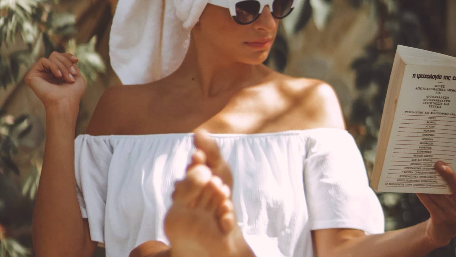 Frau entspannt in Sommer-Outfit mit Sonnenbrille und Buch