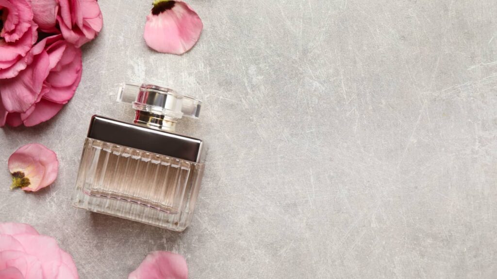 Femininer Parfum-Flakon mit Rosenblättern auf grauem Hintergrund