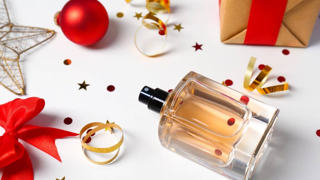 Femininer Parfum-Flakon mit Weihnachtsschmuck und Geschenken auf weißem Hintergrund
