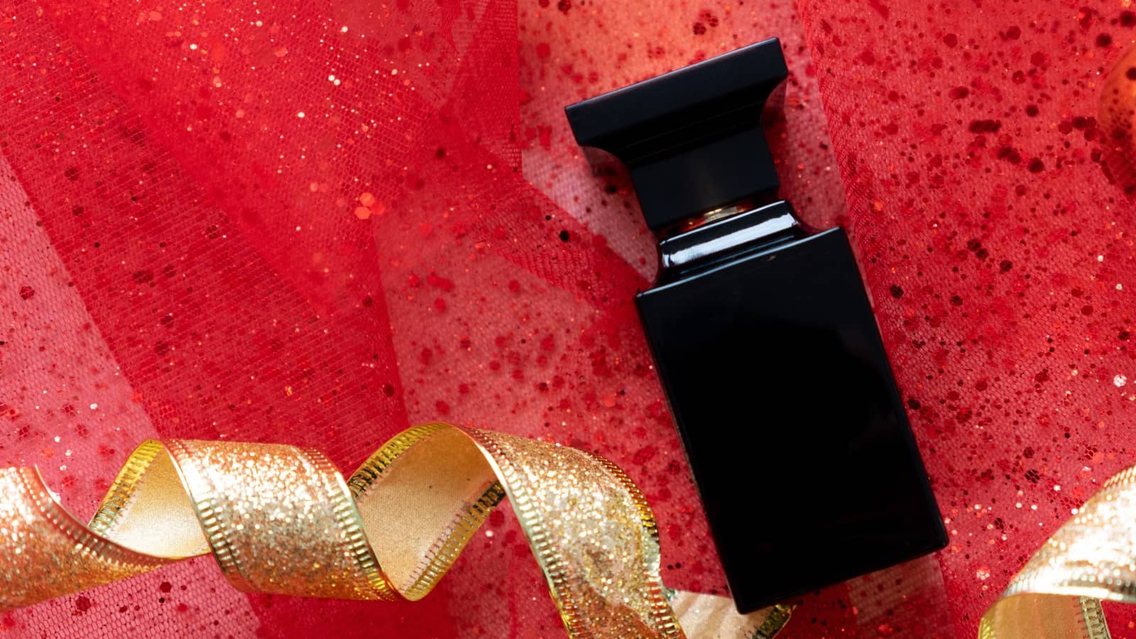 Maskuliner Parfum-Flakon mit Weihnachtsschmuck auf rotem Hintergrund